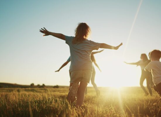 Gesundheit & Nachhaltigkeit / Health & Sustainability: Kinder laufen über eine Wiese im Sonnenuntergang, dies soll an Reflexion, Fokus auf das Wesentliche sowie einen achtsamen Umgang mit sich selbst und der Umwelt erinnern.